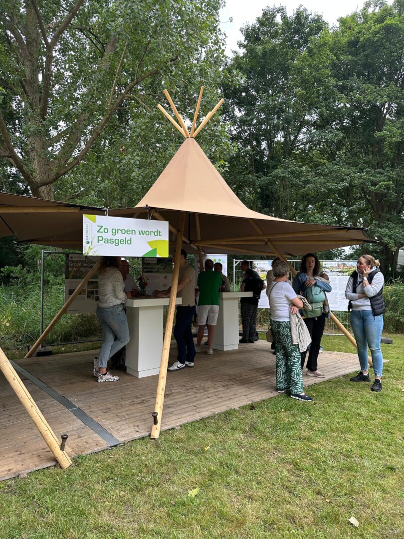 Mensen verzamelen zich rond een tent in een groene, natuurlijke omgeving.